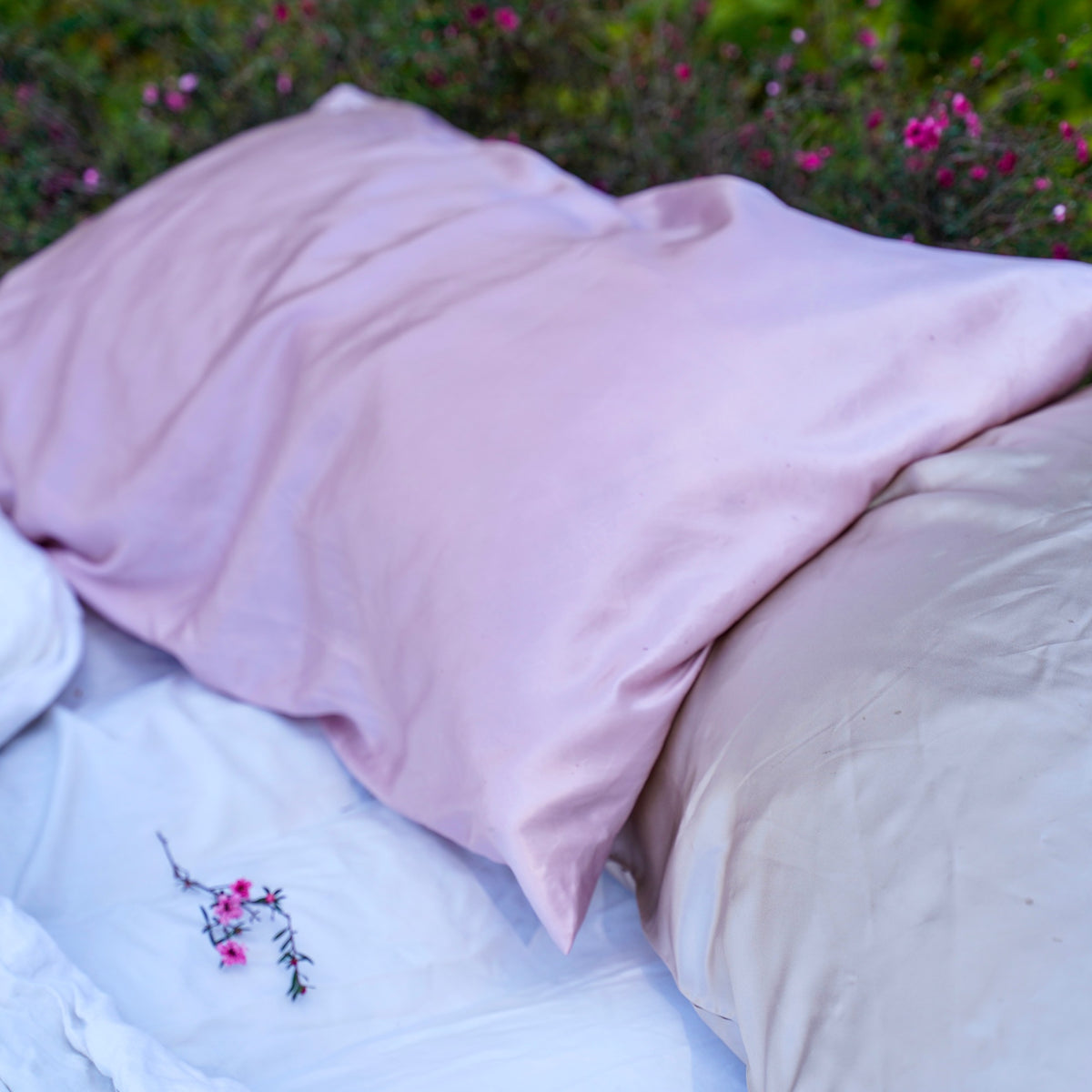 Pink and beige pillows on white bedding with scattered flowers