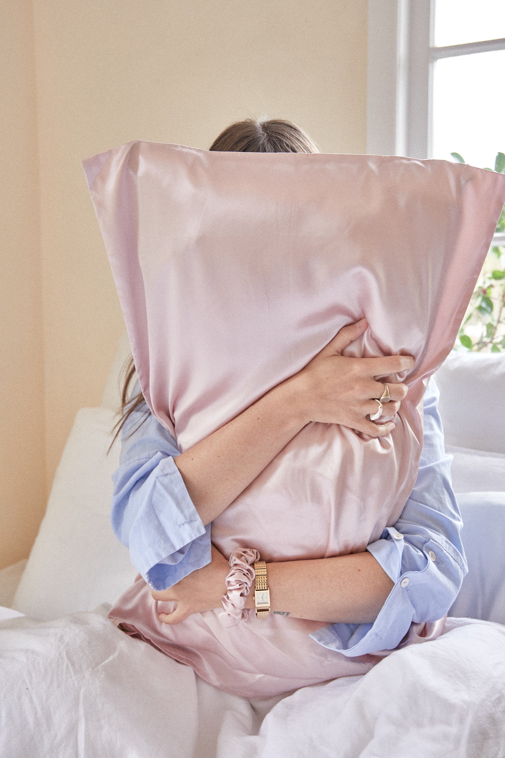 Person hugging pink satin pillow on bed in a calm, cozy setting