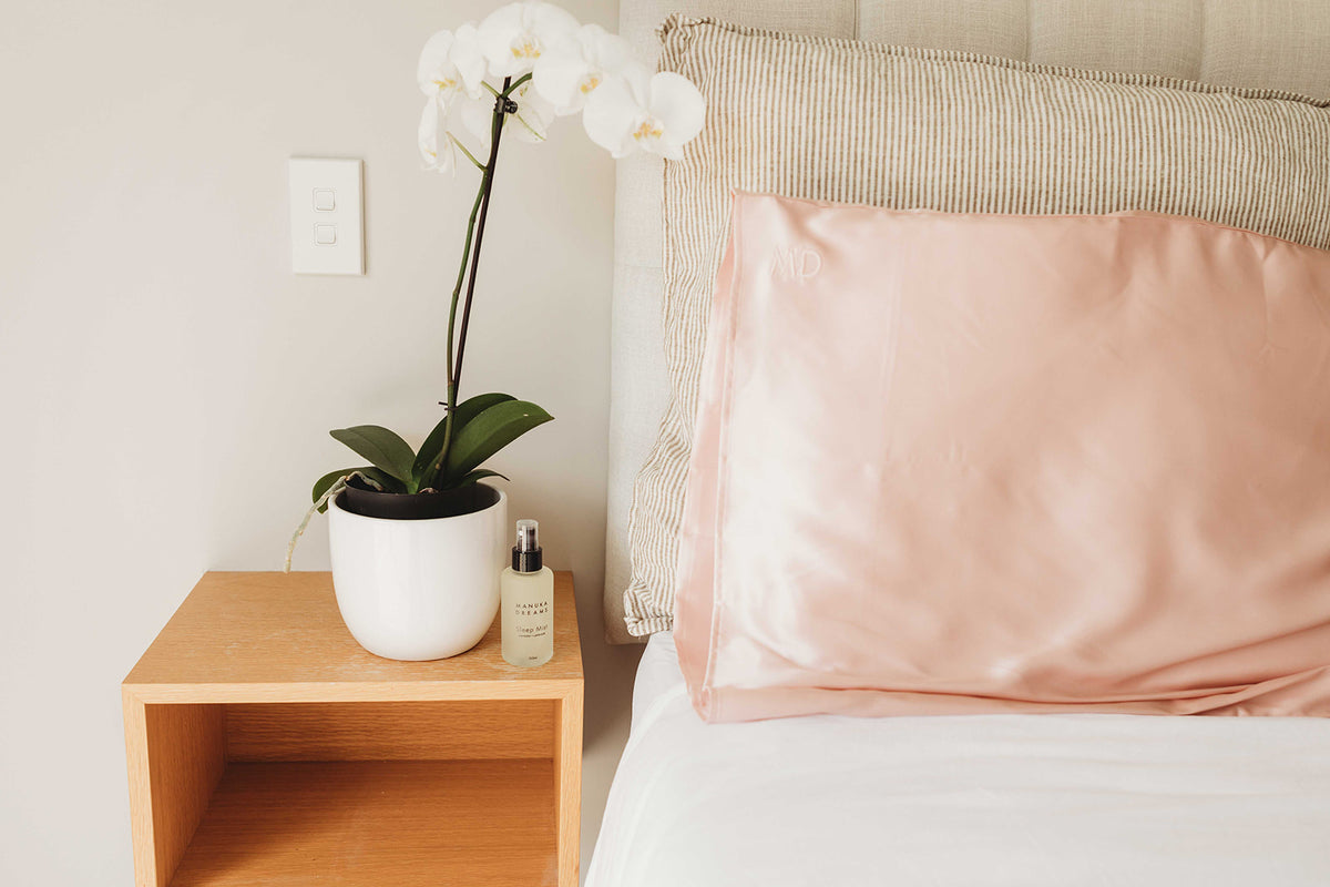Bed with pink silk pillow and striped cushion near orchid stand