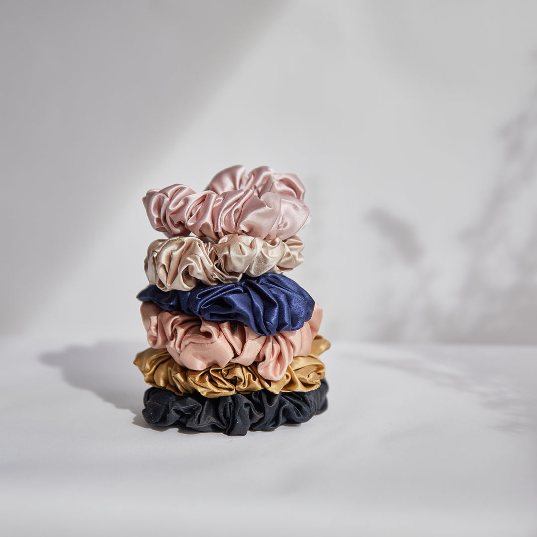 Stack of satin scrunchies in six colors on clean white surface